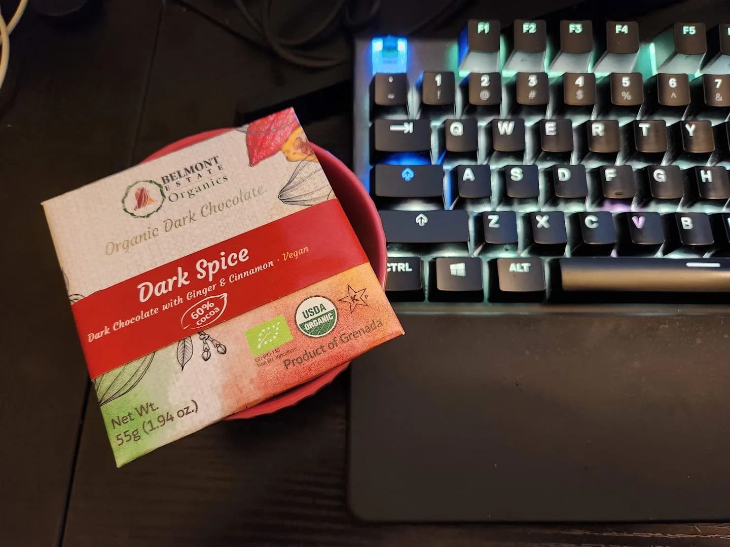 Dark chocolate package in a red dish beside an illuminated mechanical keyboard.
