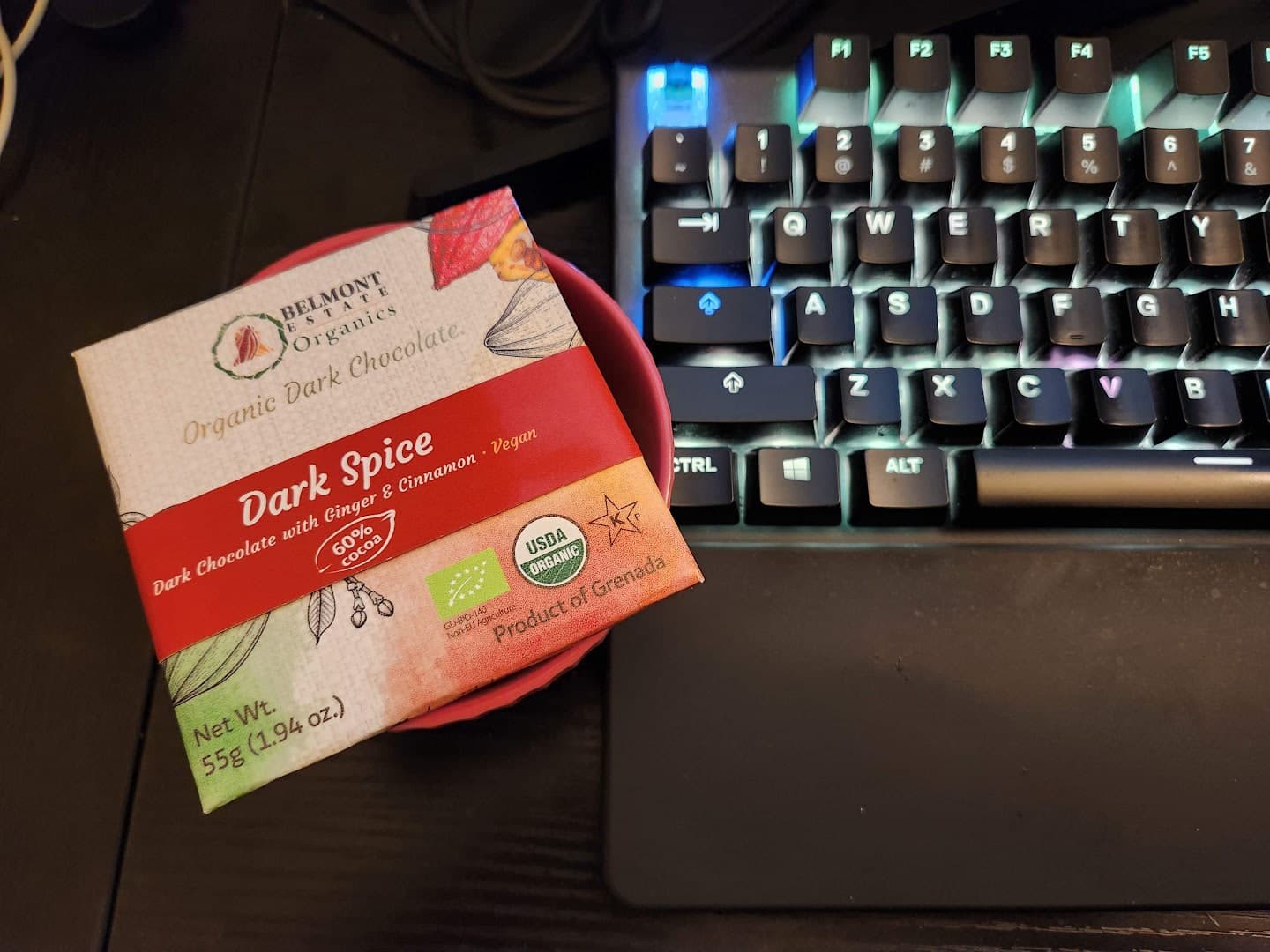 Dark chocolate package in a red dish beside an illuminated mechanical keyboard.