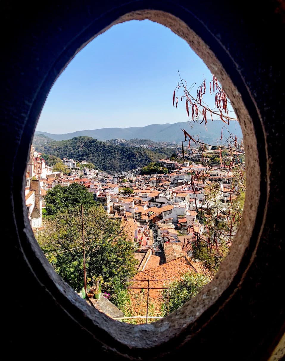 Hillside town and distant mountains framed by an oval stone opening.