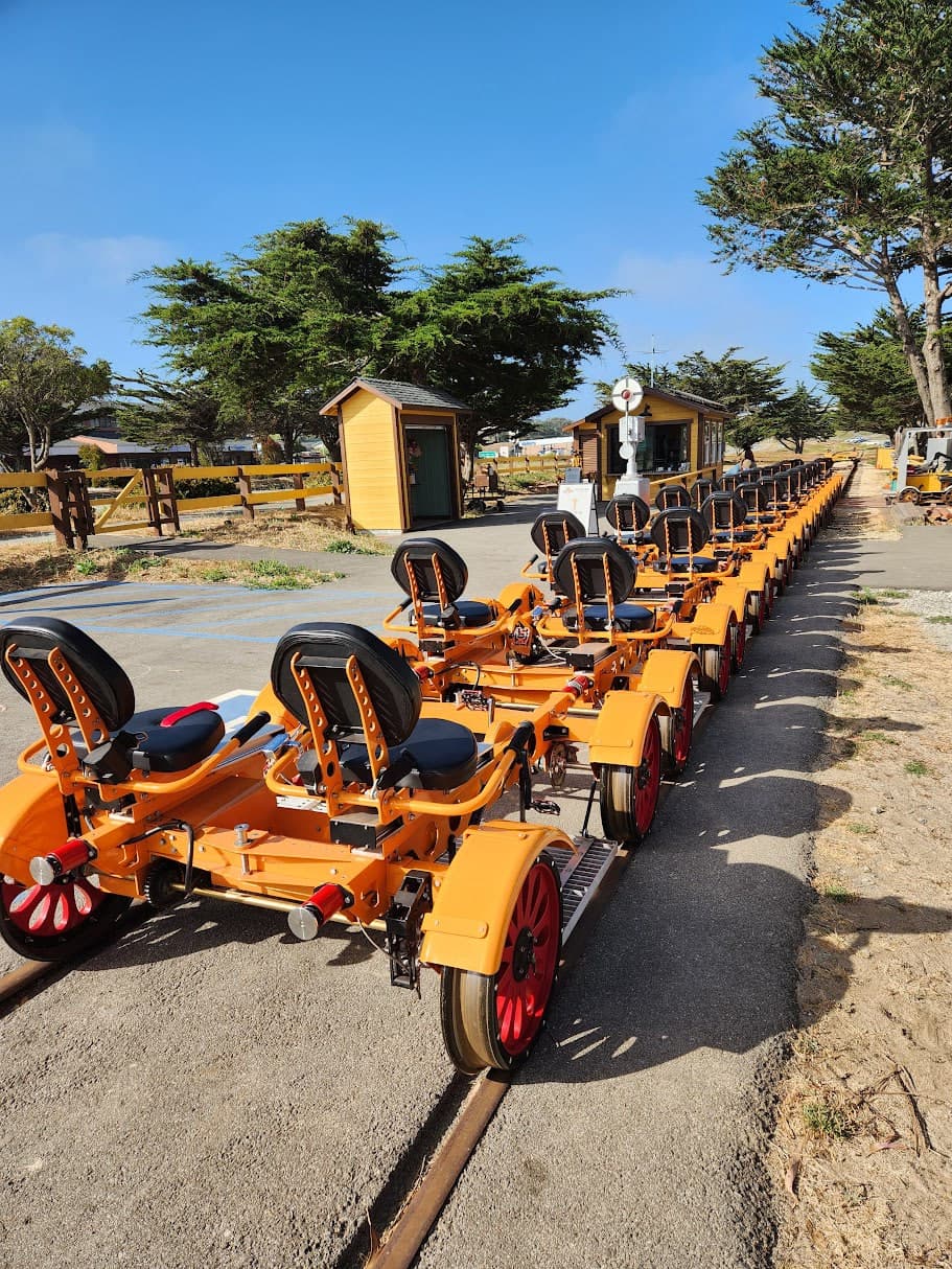 Rows of orange pedal rail carts lined up on tracks beside two small buildings.
