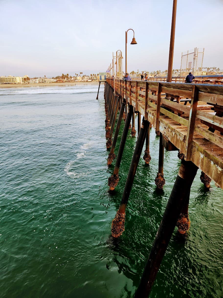 Weathered wooden fishing pier over green-blue water, lined with curved lamp posts.
