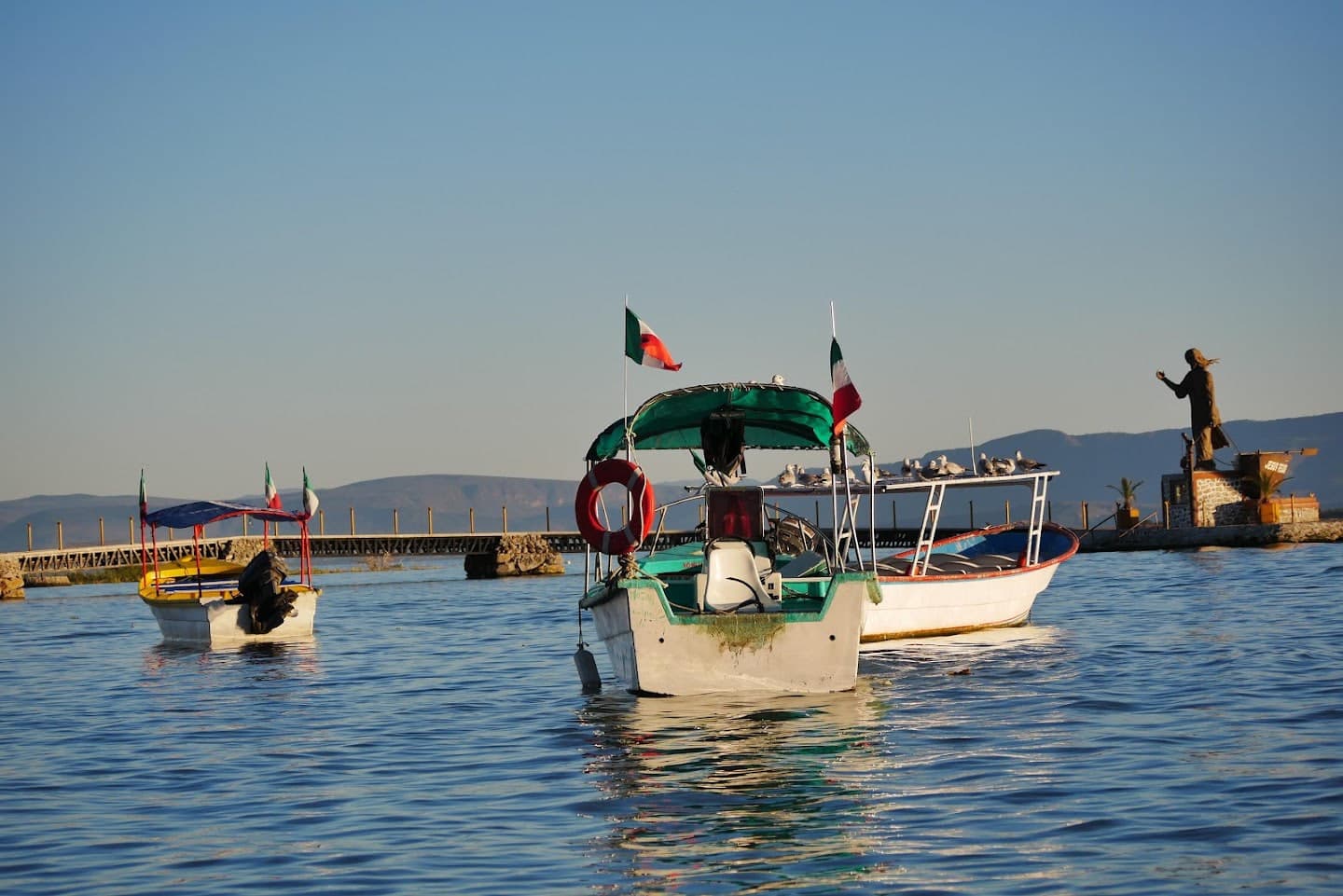 Three small boats with canopy roofs and flags floating near a stone pier.