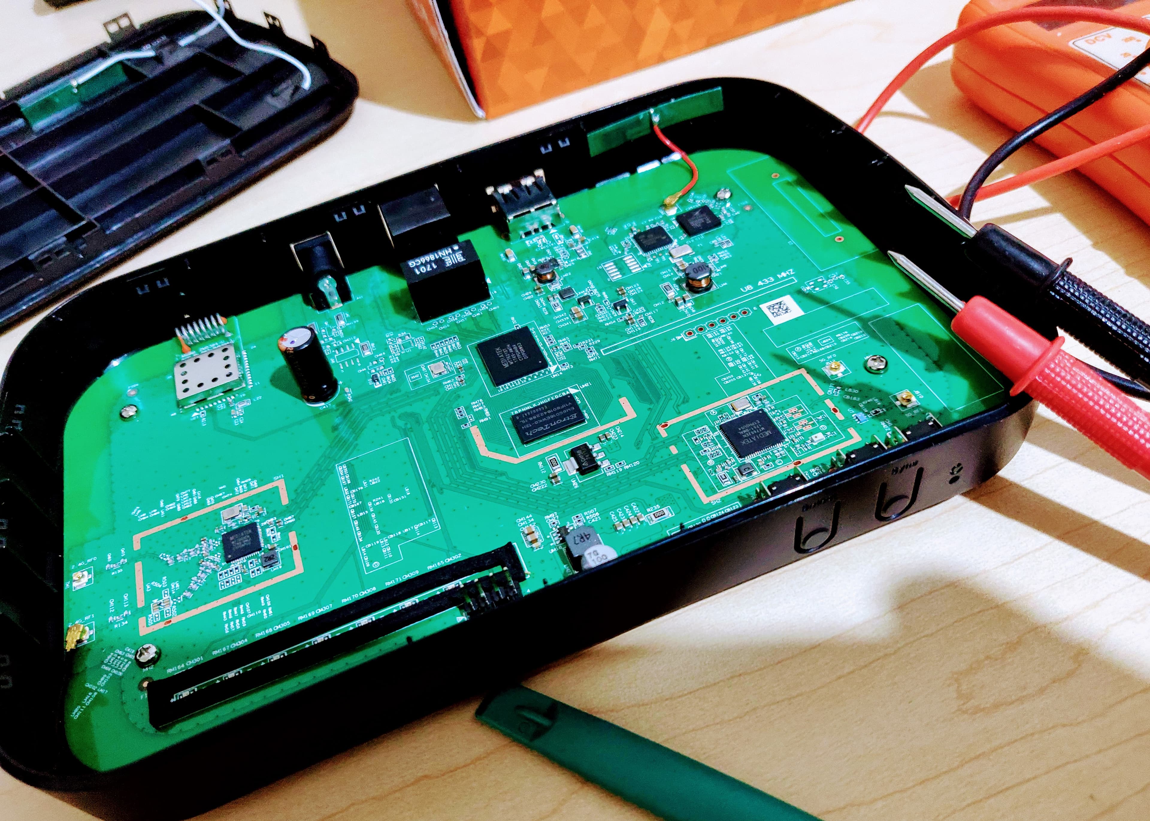 Opened networking hardware with exposed circuitry and probes attached.